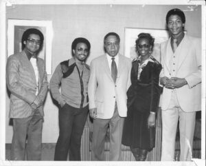 In 1977, Dr. Motley (far right) invited Alex Haley (center), “Roots” author, to the Institute. Haley lectured on his novel and its television adaption and attended a reception with students and staff. John D. O’Bryant African American Institute Special Collections.