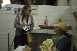 Becca is giving her speech about the documentary to a woman at the market while handing out flyers 